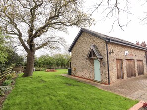 A brick building with a green door, a basketball hoop, and a large tree in the foreground. - Barn Owl Annex (Market Rasen)
