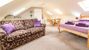Une chambre mansardée chaleureuse et bien éclairée, avec un lit en bois, un canapé à motifs et un coin repas.