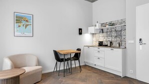 A compact kitchen with a herringbone floor pattern, white cabinetry, and a small dining area with a wooden table and black chairs. - Swan Double Studio for 2 (Reykjavík)