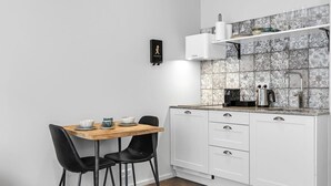A compact kitchen with white cabinets, a wooden table, black chairs, and a tiled backsplash. - Swan Double Studio for 2 (Reykjavík)