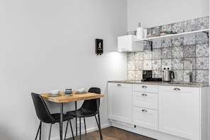 A compact kitchen with white cabinets, a wooden table, black chairs, and a tiled backsplash. - Swan Double Studio for 2 (Reykjavík)