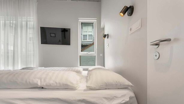 A hotel room with a bed, a window, and a wall-mounted light fixture. - Swan Double Studio for 2 (Reykjavík)