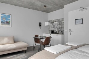 A modern hotel room with a sofa, a dining table with chairs, a kitchenette, and a bed with towels. - Swan Double Studio for 2 (Reykjavík)