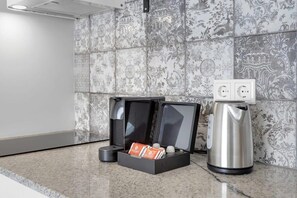 Eine Kaffeemaschine, ein Wasserkocher und eine Schachtel mit Kaffeekapseln auf einer Arbeitsplatte.