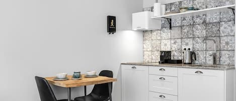 A compact kitchen with white cabinets, a wooden table, black chairs, and a tiled backsplash.