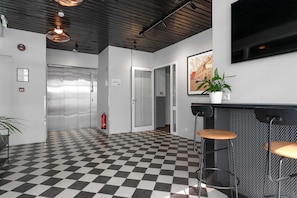 Experience the stylish lobby with a checkered floor, elevators, and a staircase, plus a cozy seating area with a flat-screen TV.