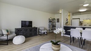 A modern living room with a flat-screen TV, a sofa, a coffee table, and a dining area with chairs and a small table. - Resort Living on the Coconut Coast (Kapaa)