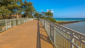A wooden boardwalk with decorative railings, leading to a beach with clear blue water and trees. - Resort Living on the Coconut Coast (Kapaa)