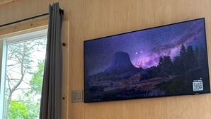 A room with a large window, a mounted TV displaying a starry night scene, and a leather sofa. - THIS IS THE ONE! SHIPPING CONTAINER CABIN-VIEW-WIFI-NATURAL BRIDGE-NADA TUNNEL (Stanton)