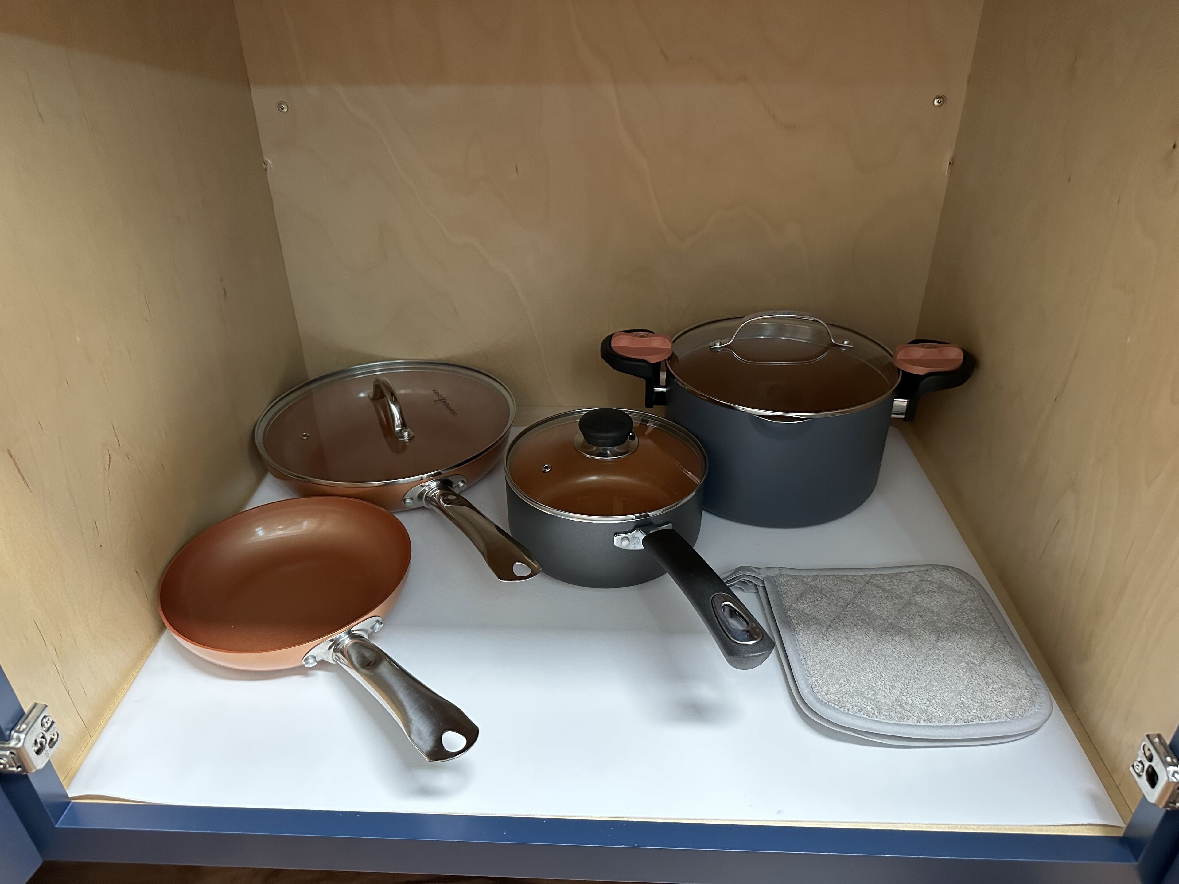 Una cocina con encimera blanca, sartén marrón, cacerola gris y olla gris con tapa.