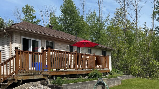 Une maison avec une terrasse en bois, un parasol rouge et un espace recouvert de gravier.