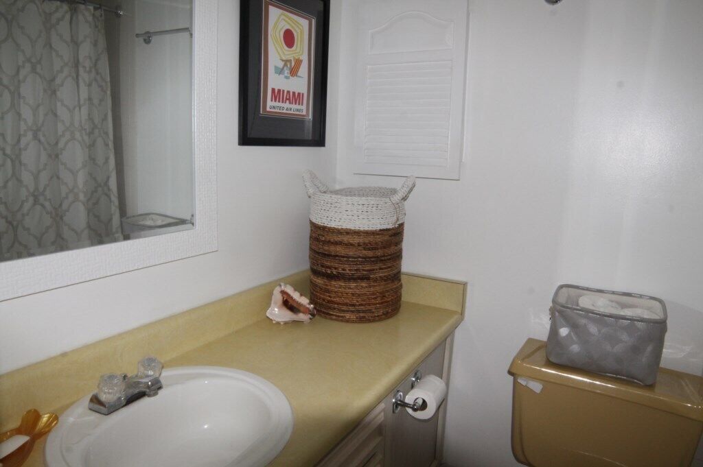 Une salle de bain équipée d’un lavabo, de toilettes et d’une affiche encadrée de la compagnie aérienne Miami United Air Lines.