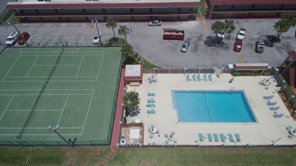An aerial view of a hotel with a tennis court, a swimming pool, and a parking lot.
