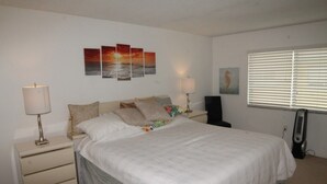 A bedroom with a bed, nightstands, a lamp, a heater, and artwork on the wall. - Pelican Inlet C218 2 Bedroom Condo by RedAwning (St. Augustine)
