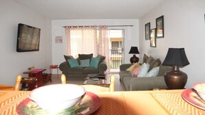 A living room with two sofas, a coffee table, and a dining table with plates and bowls. - Pelican Inlet C218 2 Bedroom Condo by RedAwning (St. Augustine)
