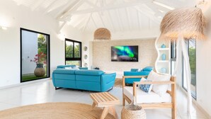 A modern living room with a large sofa, a smaller sofa, a wooden coffee table, and a TV mounted on the wall. - Superbe Villa vue mer (Sainte Anne)