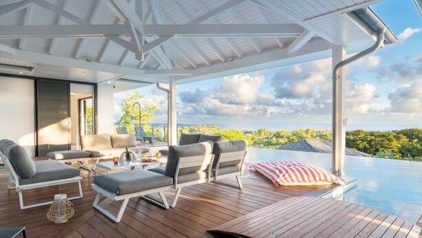 A modern outdoor lounge area with a pool, wooden deck, and seating. - Superbe Villa vue mer (Sainte Anne)