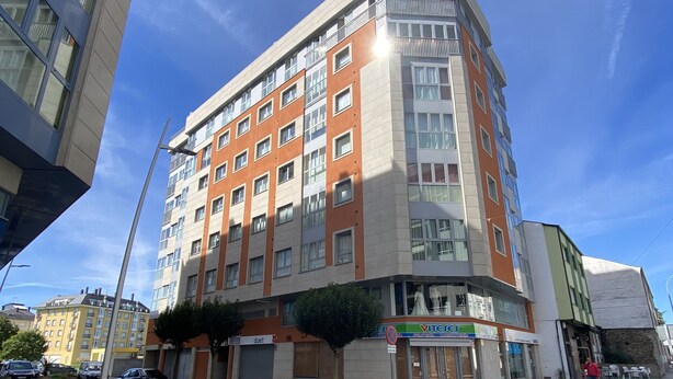 Ein mehrstöckiges Hotel mit modernem Design, das rote und beigefarbene Fassadelemente, große Fenster und einen gut sichtbaren Eingang mit Beschilderung kombiniert.