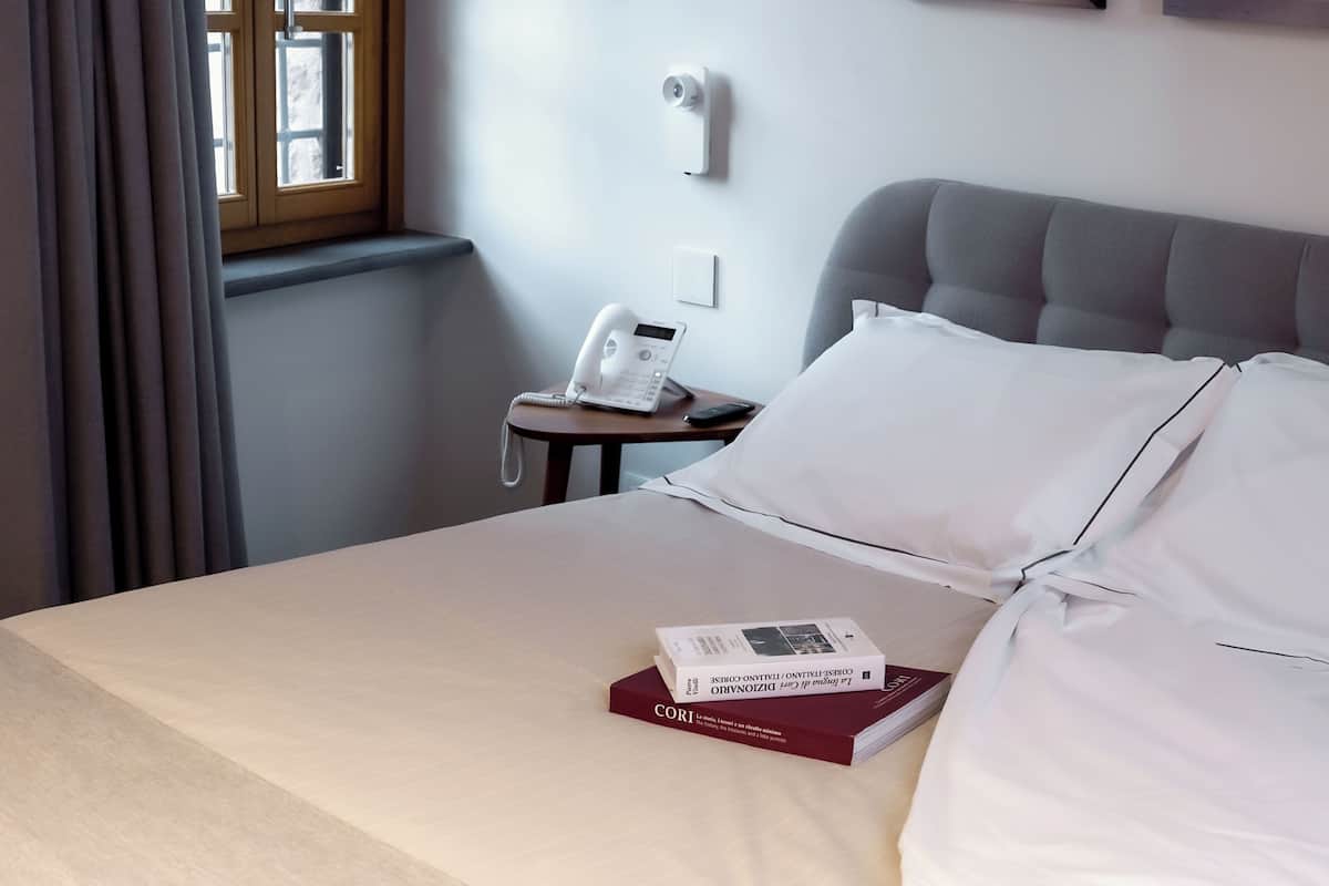 Una habitació d'hotel amb un llit, una taula de nit amb un telèfon, un llibre i una finestra amb cortines.
