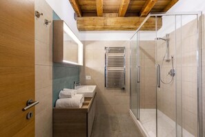 Un baño moderno con ducha de vidrio, tocador de madera, lavamanos y espejo.