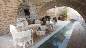 Un patio de paredes de piedra con muebles de mimbre blanco, una mesita redonda y una planta en maceta.