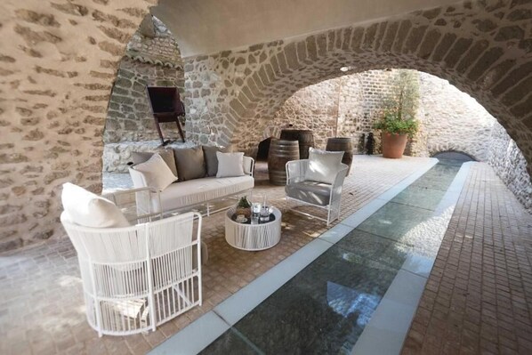 Une terrasse aux murs de pierre, agrémentée de meubles en osier blanc, d’une petite table ronde et d’une plante en pot.