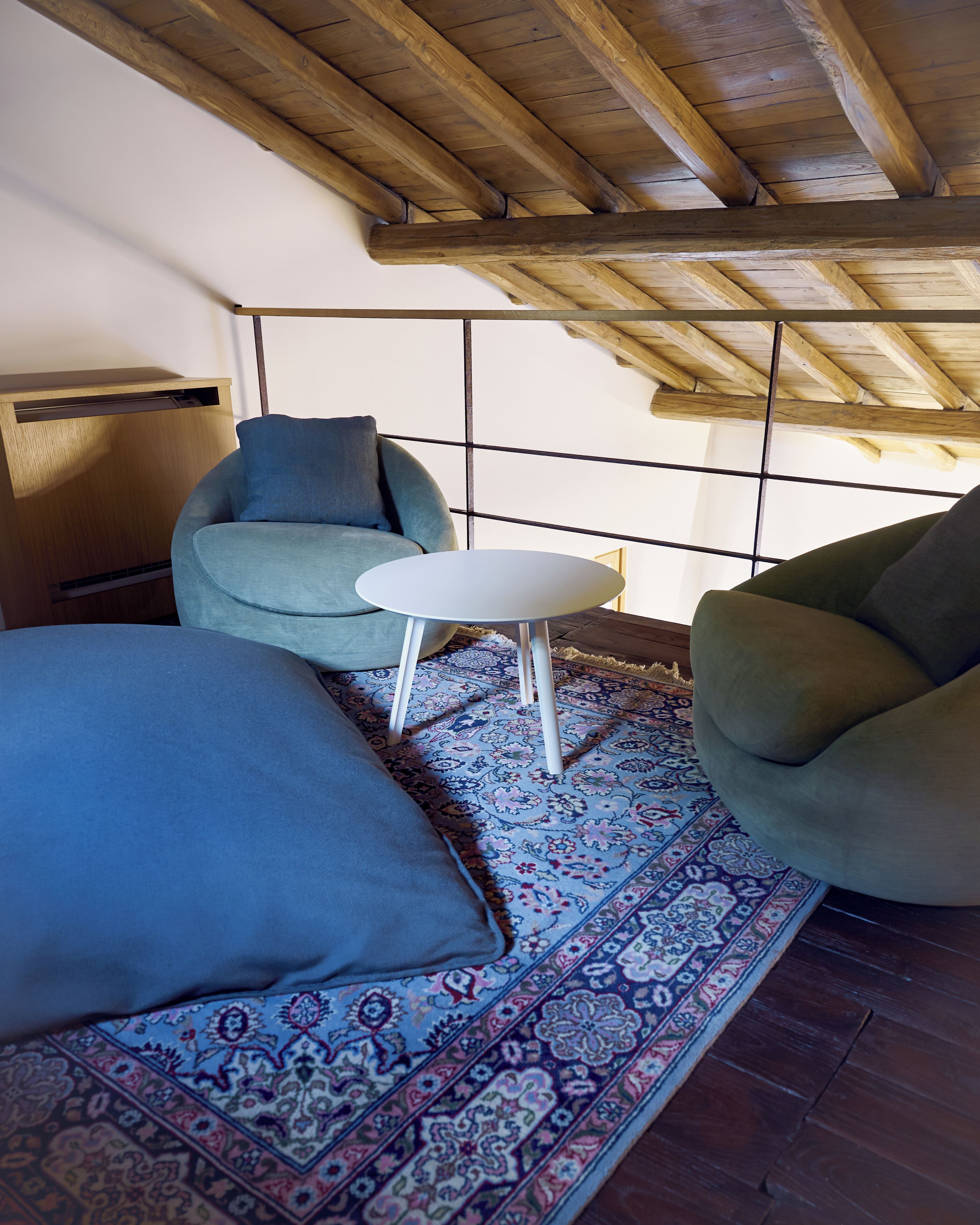A room with a wooden ceiling, a patterned rug, a blue sofa, a white table, and a green armchair.