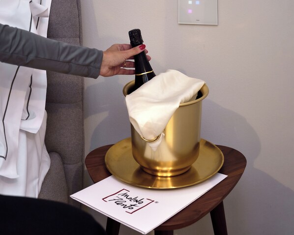 A hand holding a champagne bottle, a gold bucket, and a white cloth on a small table with a sign that reads 'Molinho Floresta.'