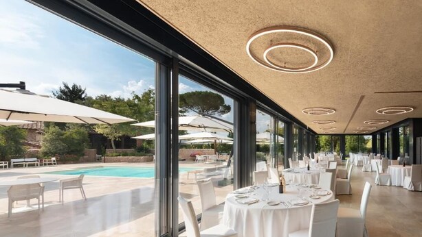 Un amplio comedor interior con ventanas grandes que dan a una piscina y asientos al aire libre.