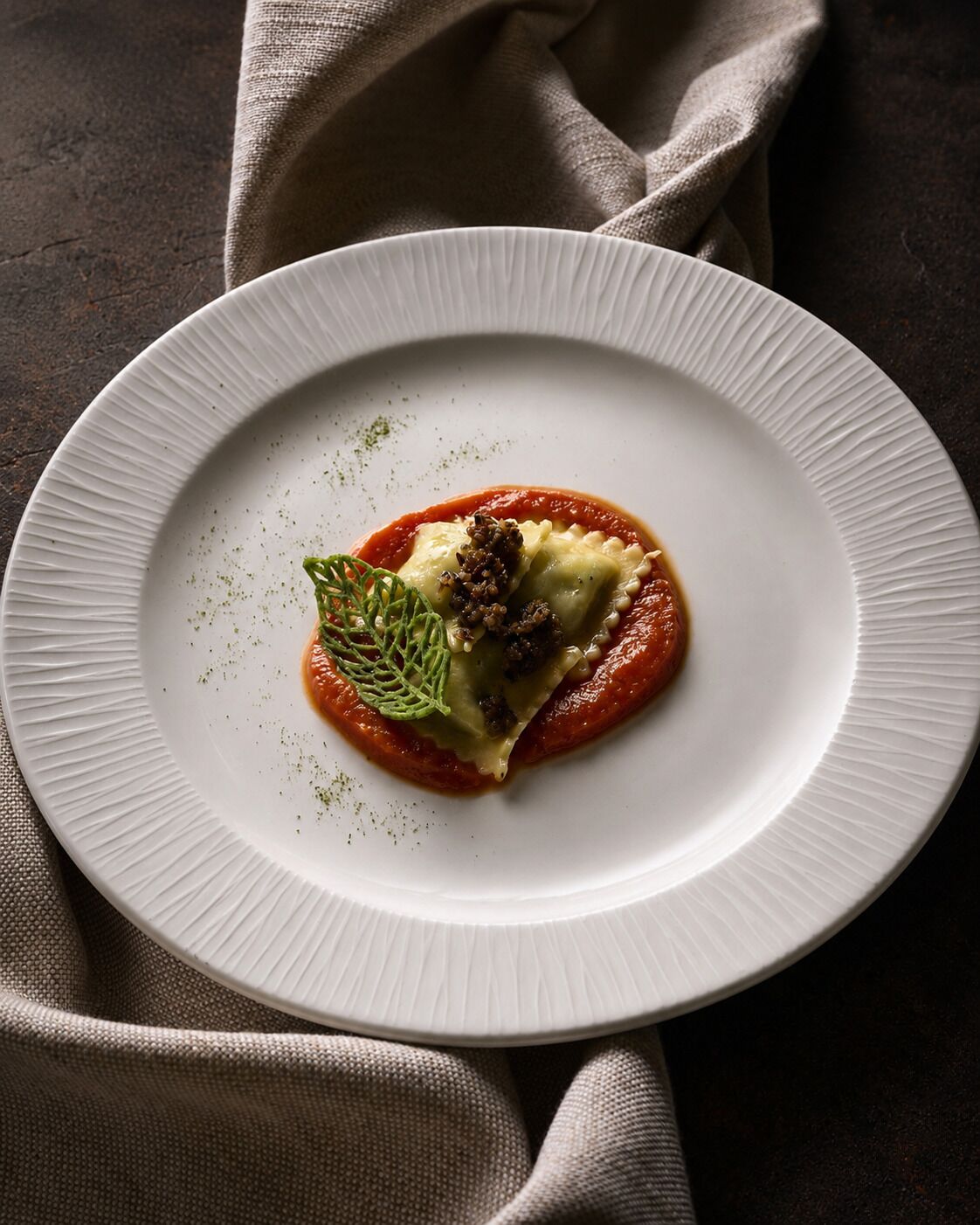 Um prato branco com ravioli, molho de tomate e um enfeite sobre uma superfície texturizada.
