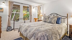 Un dormitorio con cama, dos lámparas de noche, una ventana con cortinas y un ventilador.