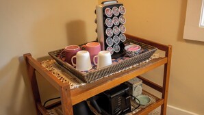Una silla de madera con una bandeja tejida que contiene tazas, una cafetera y un bol.