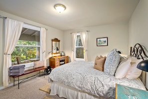 A bedroom with a large bed, a wooden dresser, a bench with towels, and a window with curtains.