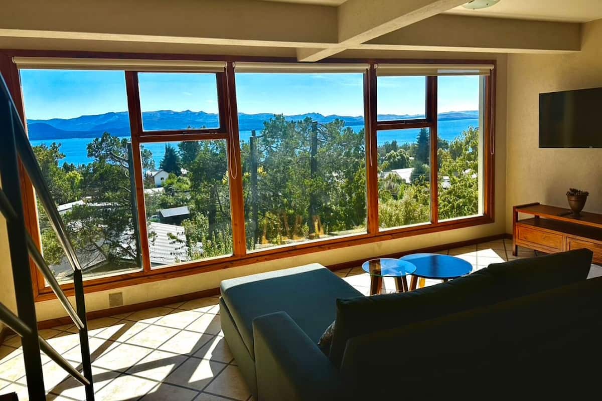 Amplia habitación con ventanas grandes que ofrecen vistas a un paisaje montañoso y una masa de agua.