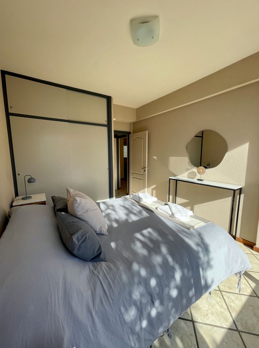 Un dormitorio con cama, mesita de noche, lámpara y espejo en la pared.