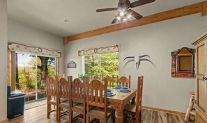 Un comedor con mesa y sillas de madera, ventilador de techo y ventana con marco decorativo.