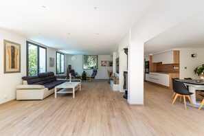 A spacious living area with a sofa, coffee table, and chairs. There is a dining table with chairs and a kitchen area with cabinets and a stove. - HappyFew La Villa Summertime (Nice)