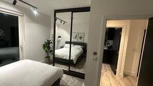 Un dormitorio moderno con una cama, una planta en maceta y un espejo que refleja otra habitación.