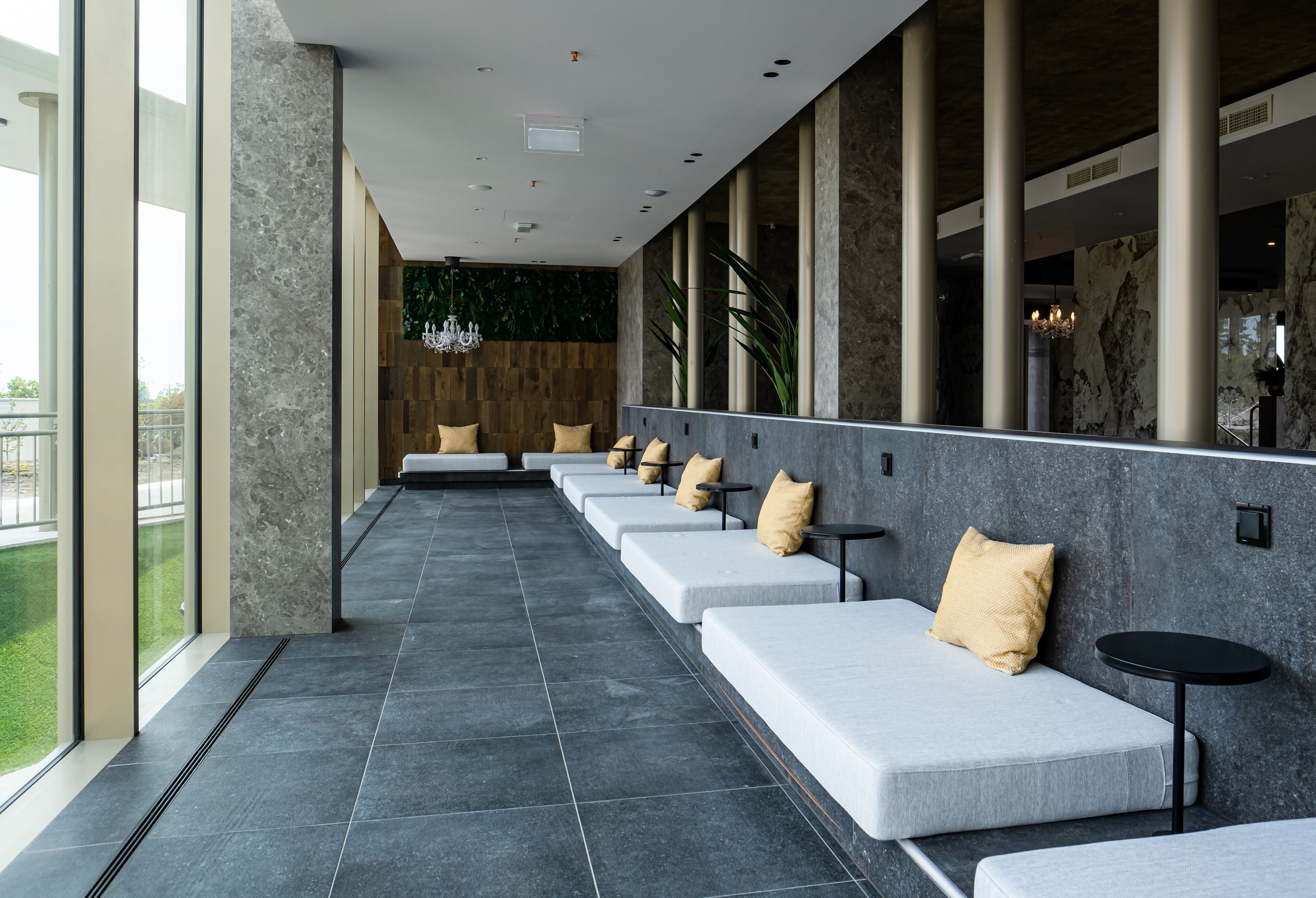 A modern lounge area with a long bench seating arrangement, large windows, and a chandelier.