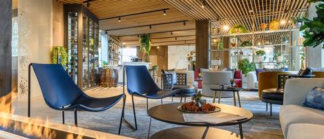 A modern interior with a central seating area featuring a round table, blue chairs, and a fire feature.