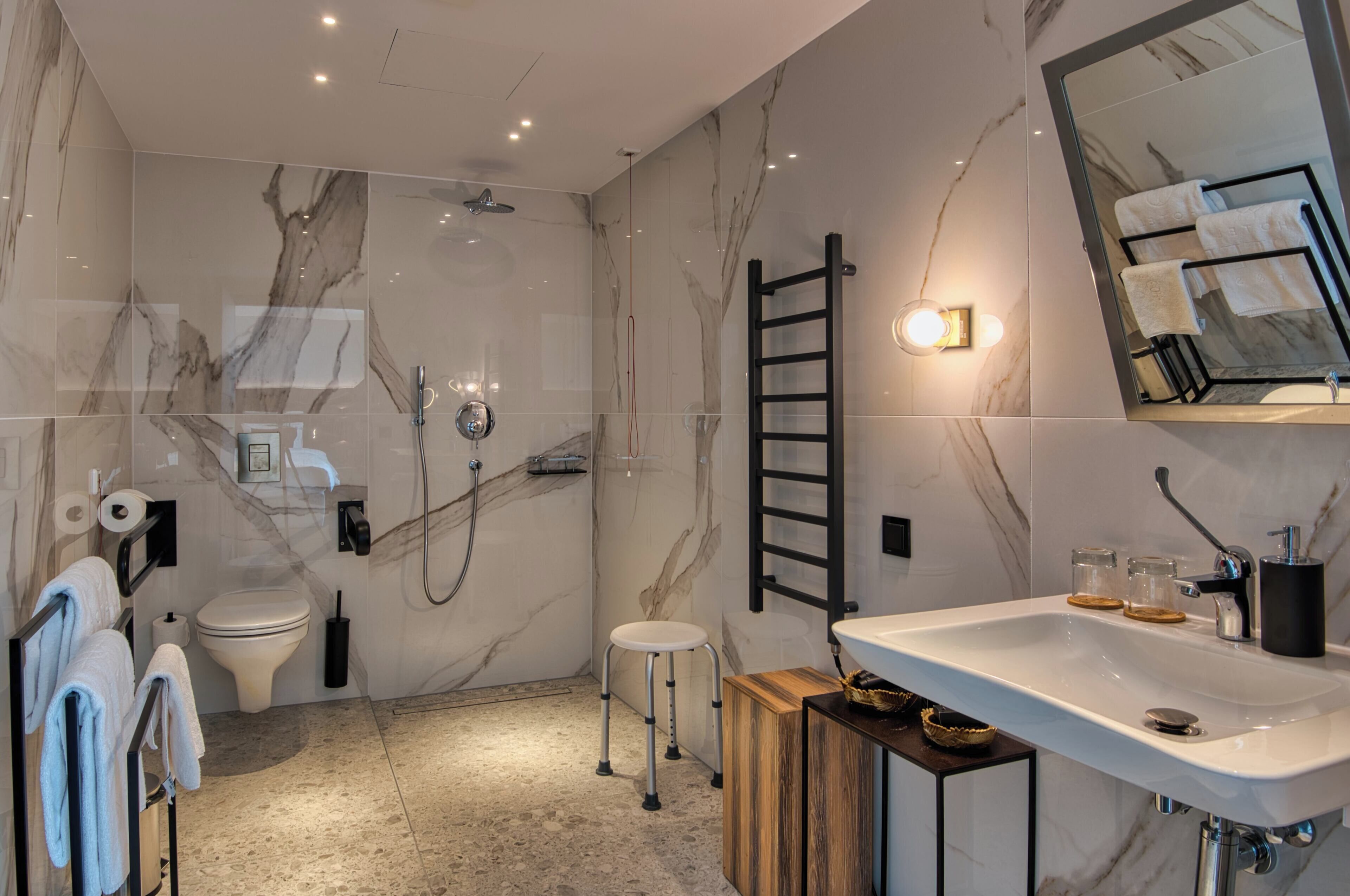 A modern bathroom with a marble floor, a shower, a toilet, a sink, and a mirror.