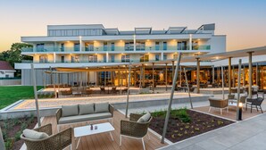 A modern hotel with outdoor seating areas, a pool, and a well-lit facade. - Hotel Vinifera Wine & Spa (Balatonfured)