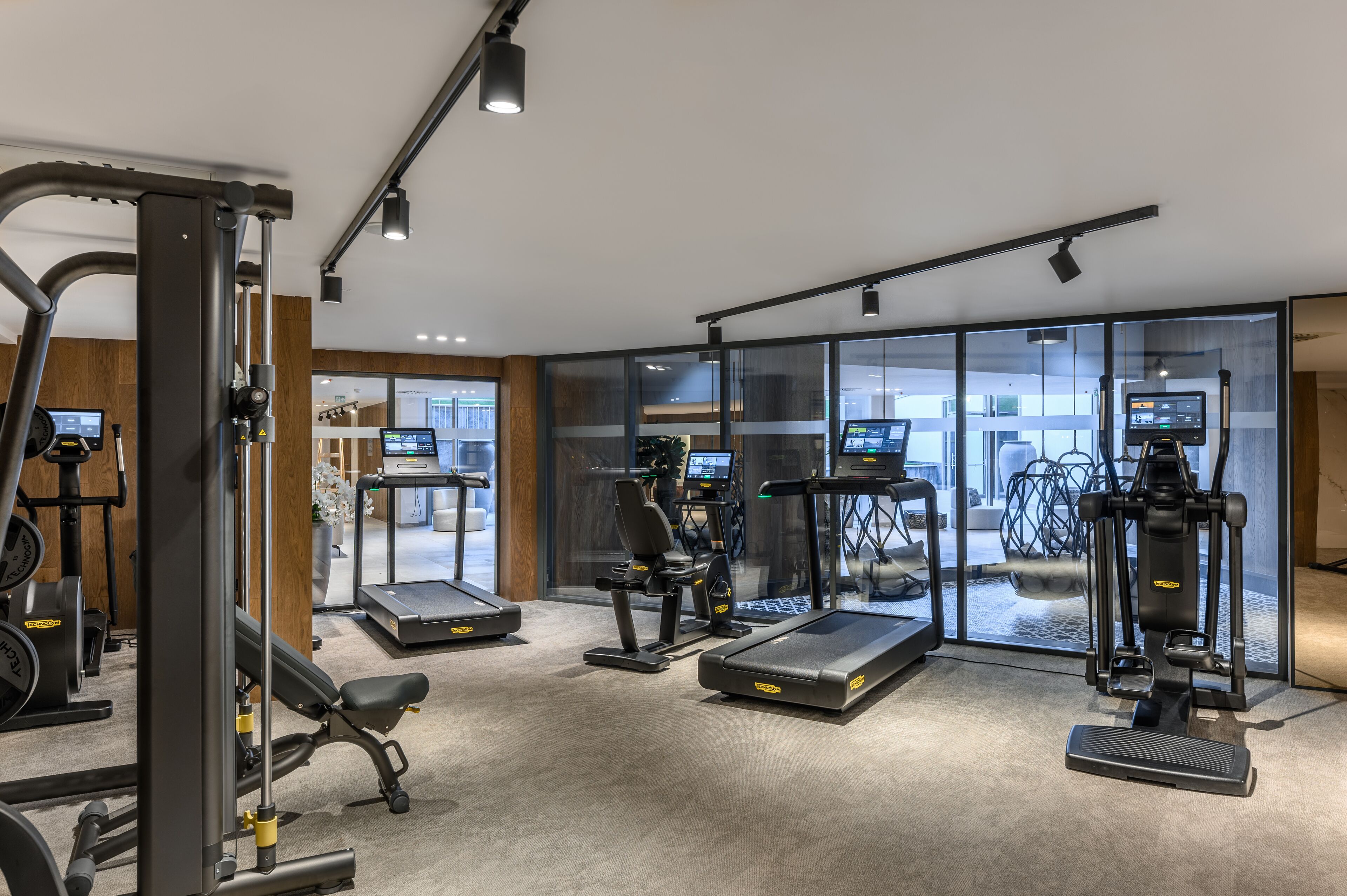A modern gym with various exercise equipment, large windows, and a clean, well-lit interior.