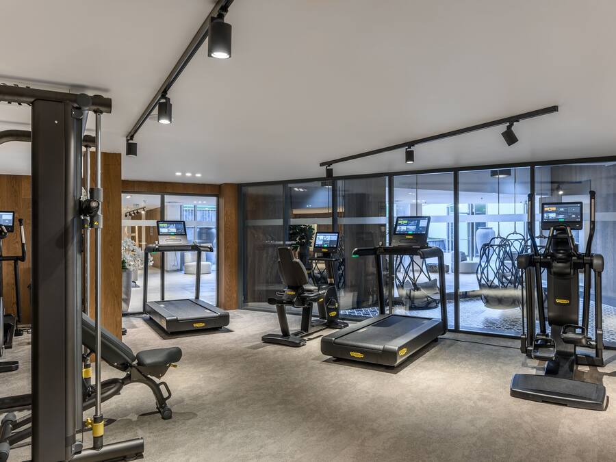 A modern gym with various exercise equipment, large windows, and a clean, well-lit interior.
