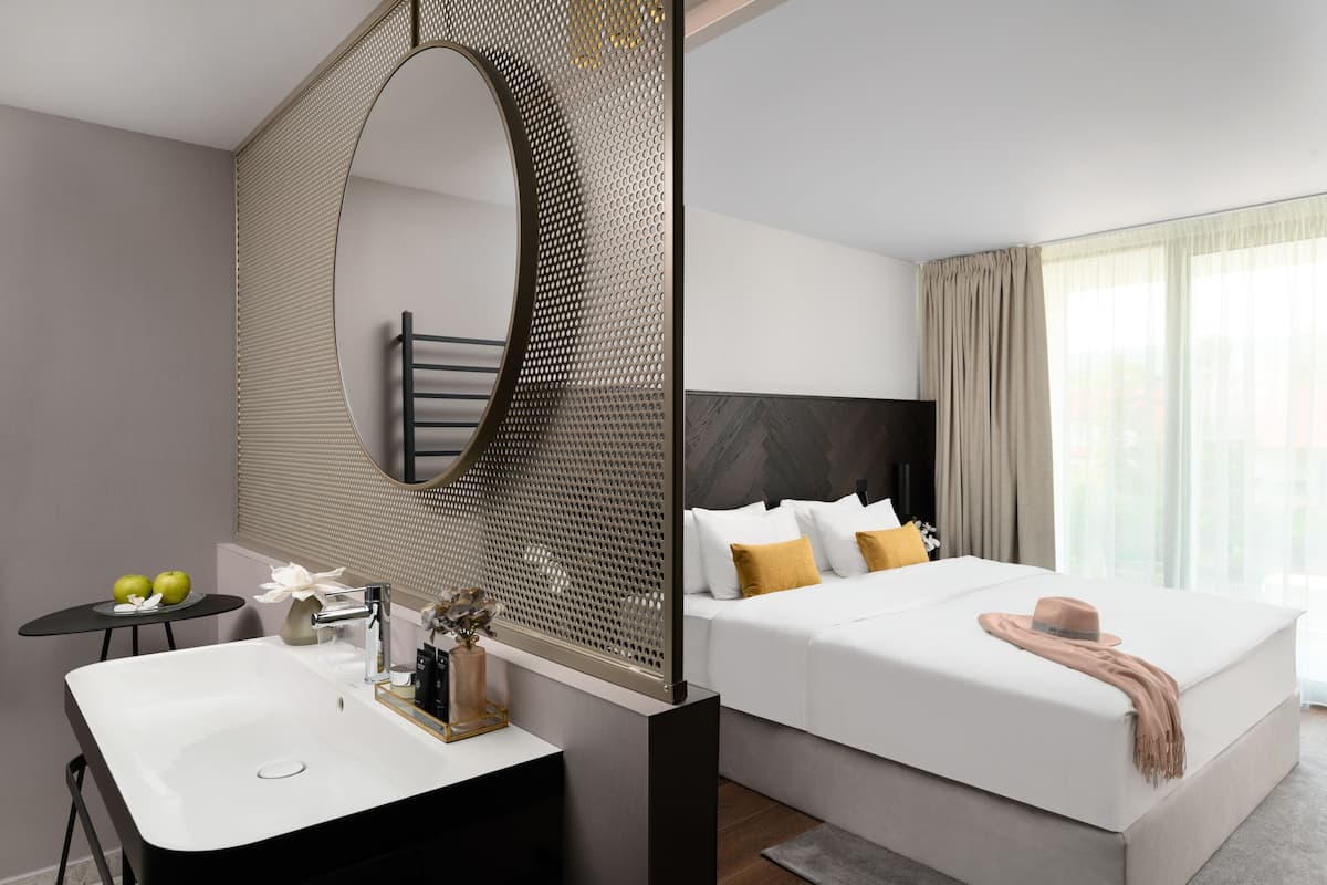 A modern hotel room with a large bed, a bathroom with a sink, and a large mirror.