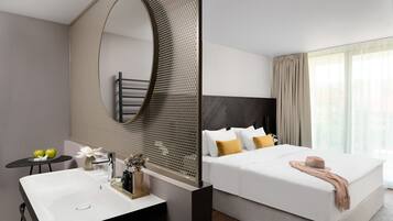 A modern hotel room with a large bed, a bathroom with a sink, and a large mirror.