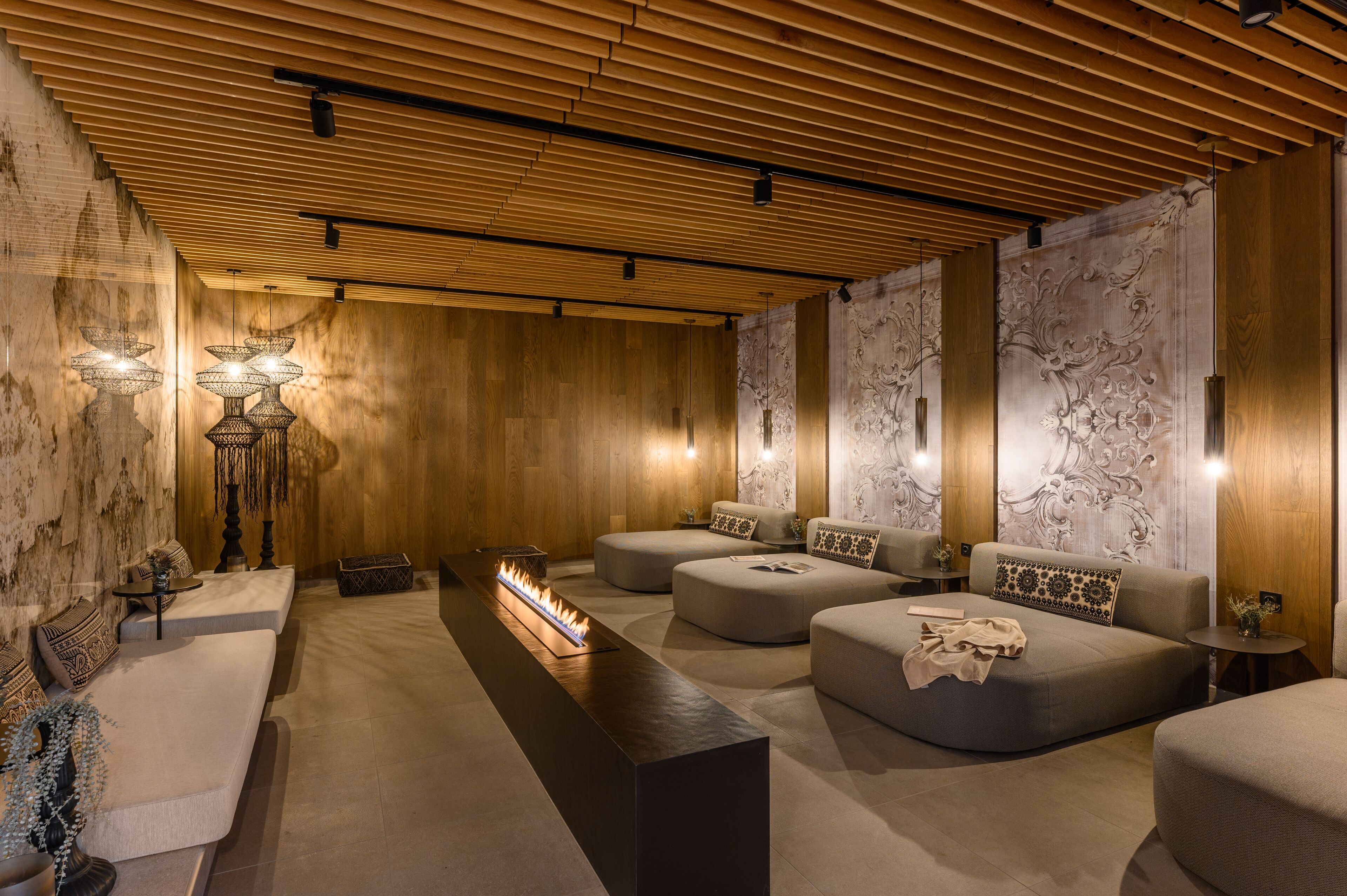A modern spa room with wooden paneling, a central heated floor, and multiple seating areas.