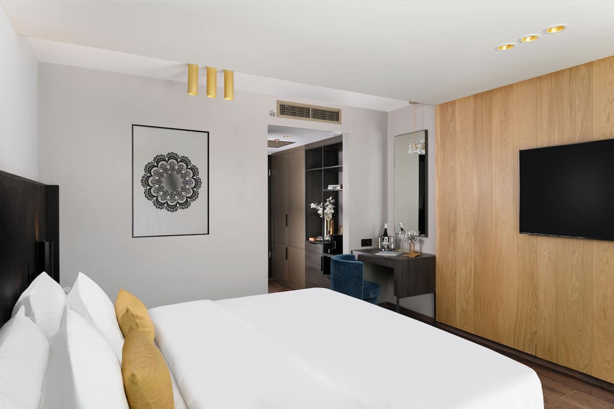 A modern hotel room with a bed, a desk, a wardrobe, and a TV.