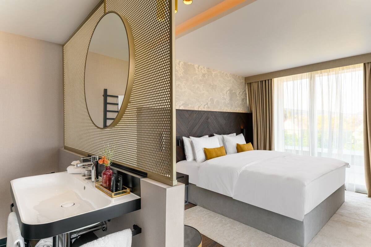 A hotel room with a large bed, a bathroom with a sink and mirror, and a view of the outdoors through the window.