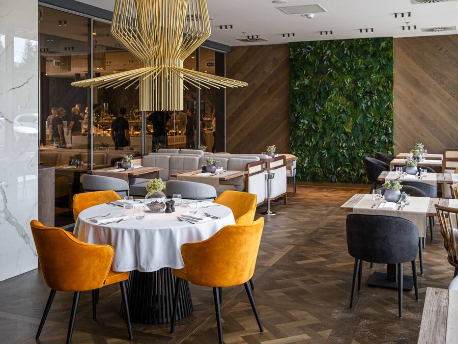 A modern restaurant with round tables, yellow chairs, and a unique ceiling light fixture.